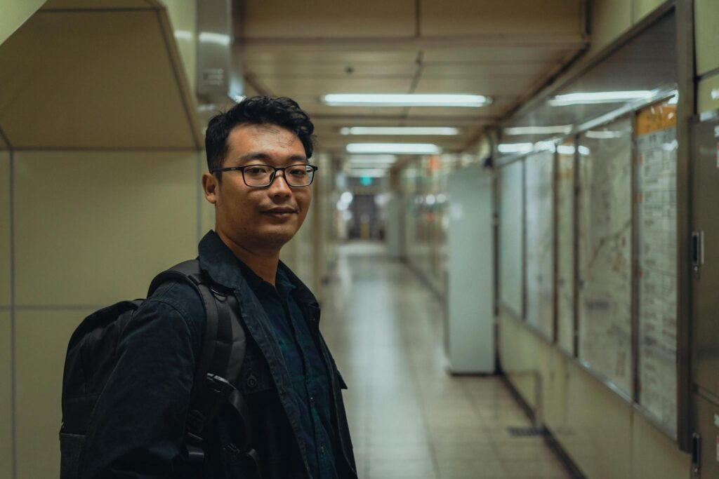 A man with glasses and a backpack in a Seoul underground corridor. A blend of urban and personal exploration.