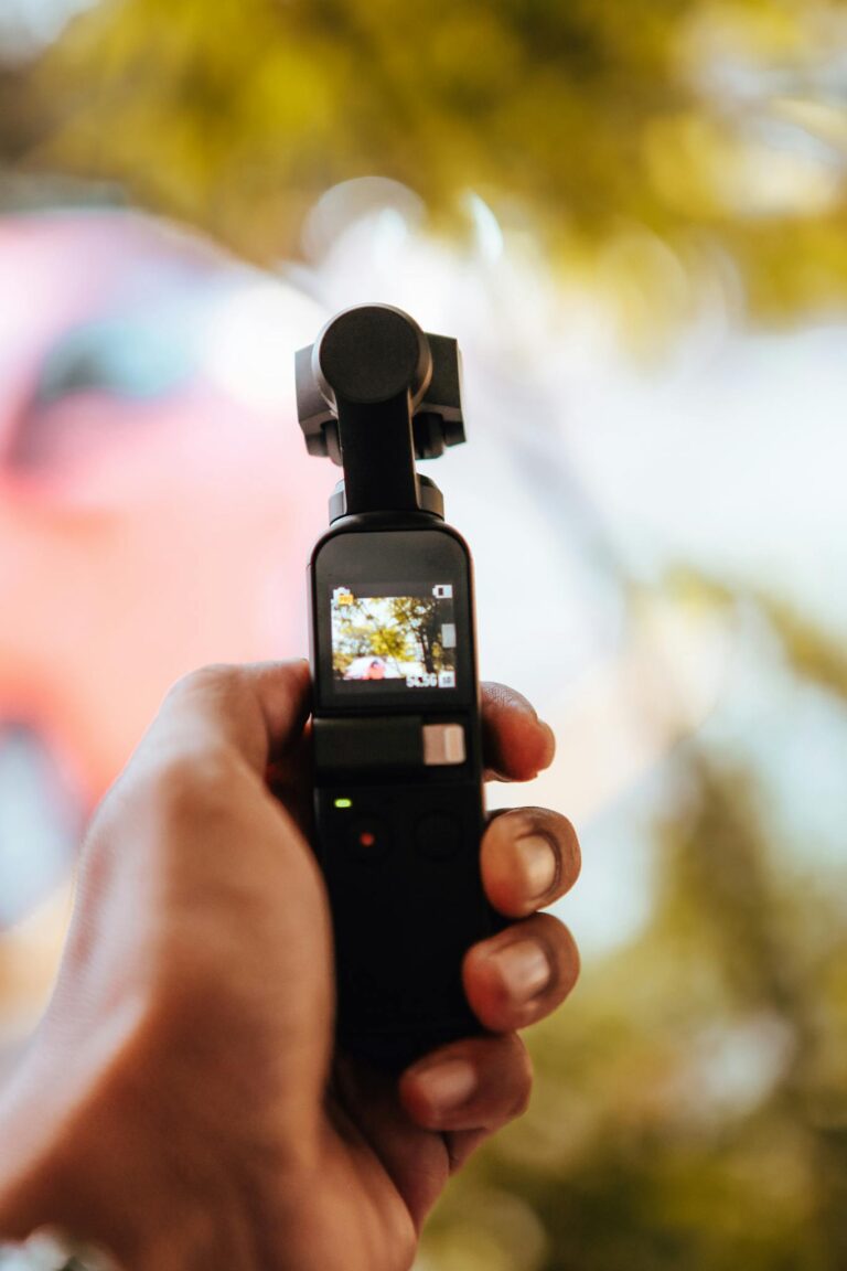 Person capturing outdoor scene with a handheld portable camera in a natural setting.